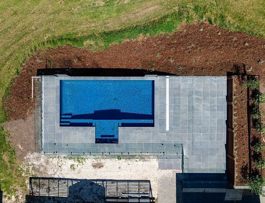 Aerial view of a rectangular blue swimming pool with concrete patio and landscaping.