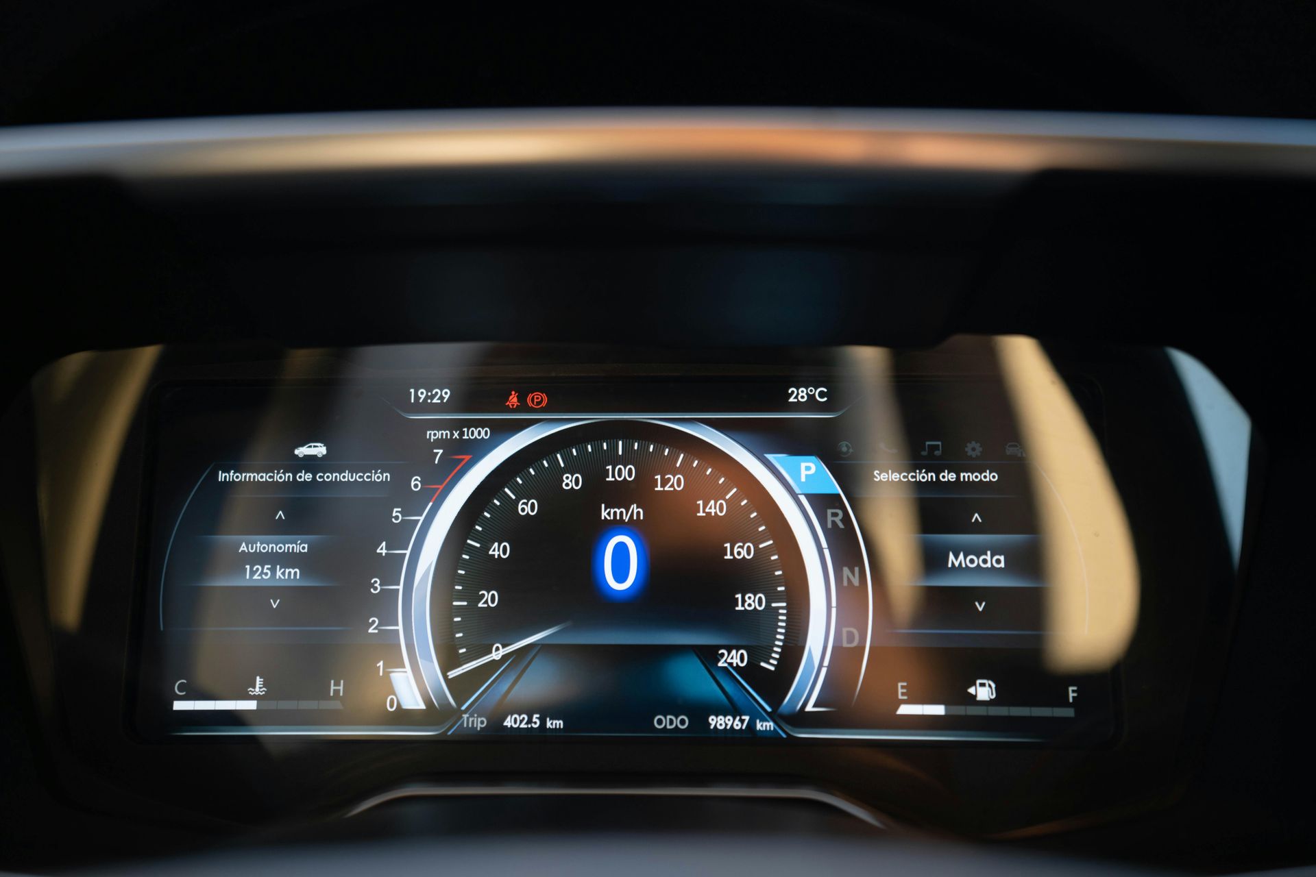 Digital car dashboard display showing speedometer at zero, fuel level, temperature, and driving information in a modern vehicle.