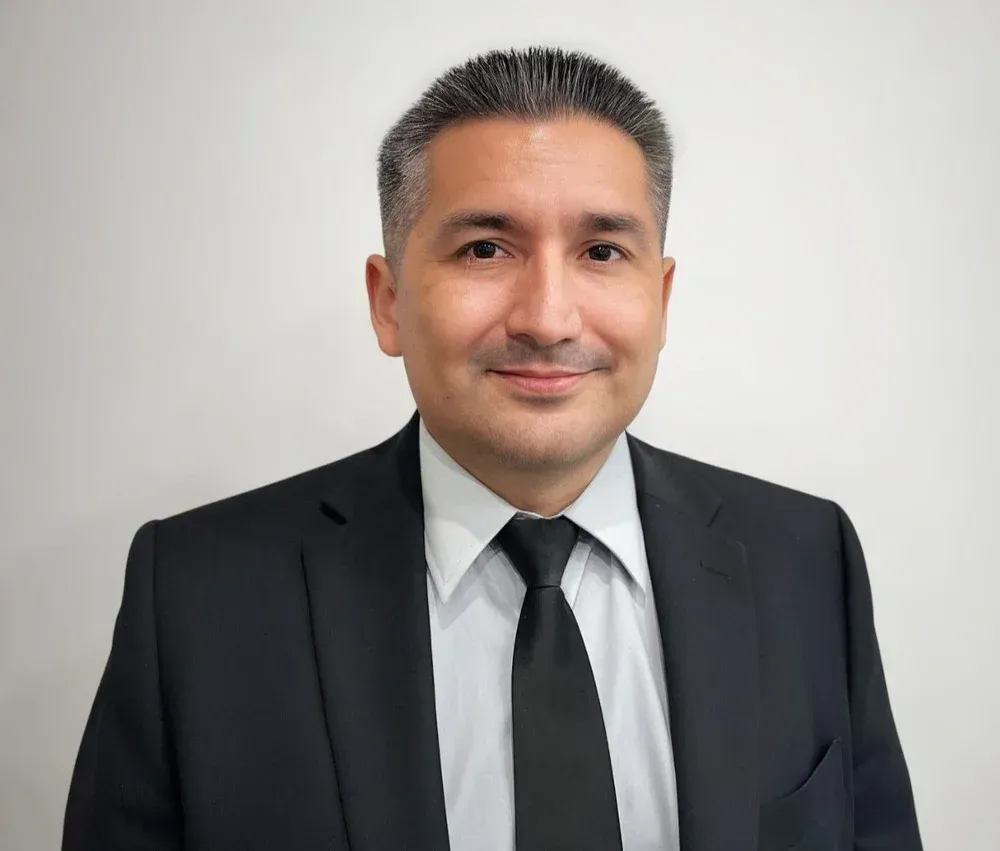 Man in suit and tie smiling, posing in front of a white wall.