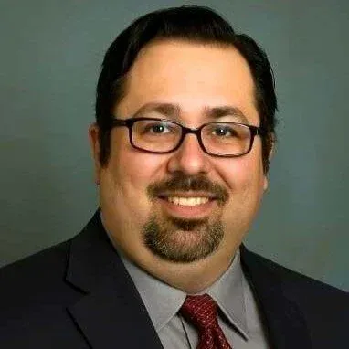 Man in glasses smiling, wearing a suit and tie.