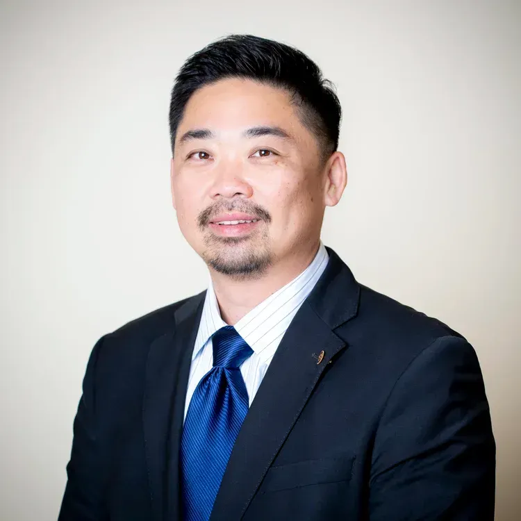 Man in a suit smiles at the camera against a neutral background.