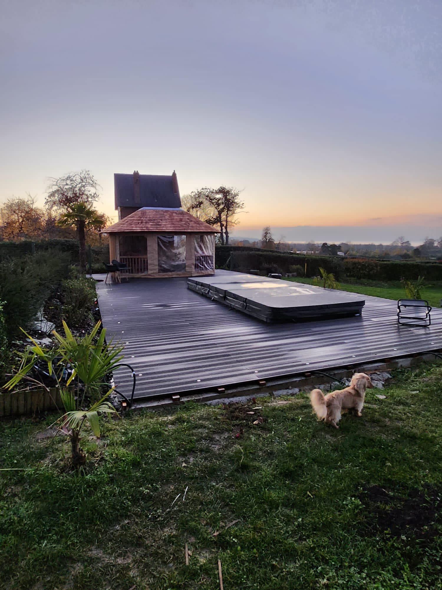 Terrasse arrière au coucher du soleil avec une plateforme surélevée, une petite maison et un chien sur la pelouse