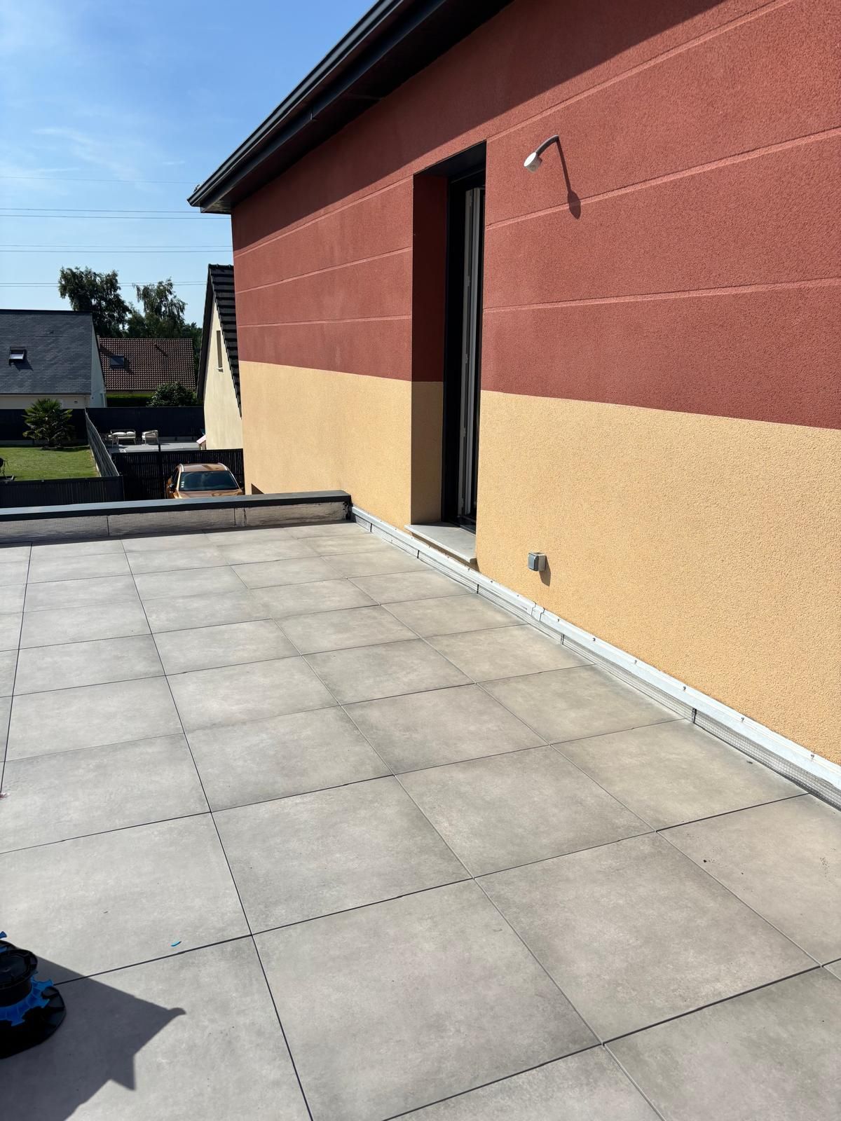 Terrasse sur le toit avec des dalles de béton à côté d'un bâtiment rouge et beige sous un ciel bleu clair