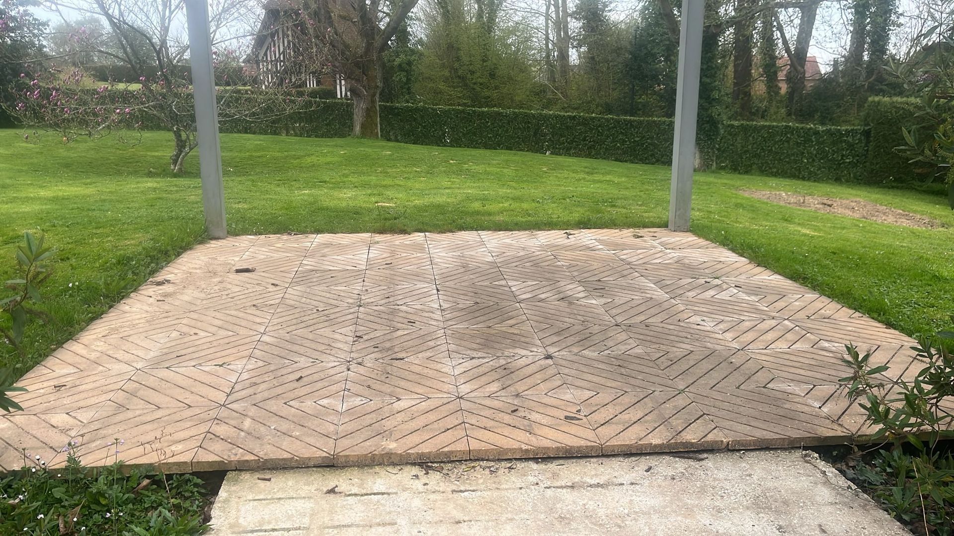 Plateforme couverte et vide dans un parc herbeux, bordée d'arbres et de poteaux en béton.