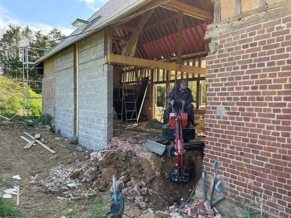Maison en briques partiellement construite, façade ouverte et débris de chantier, ouvrier utilisant du matériel rouge à l'intérieur