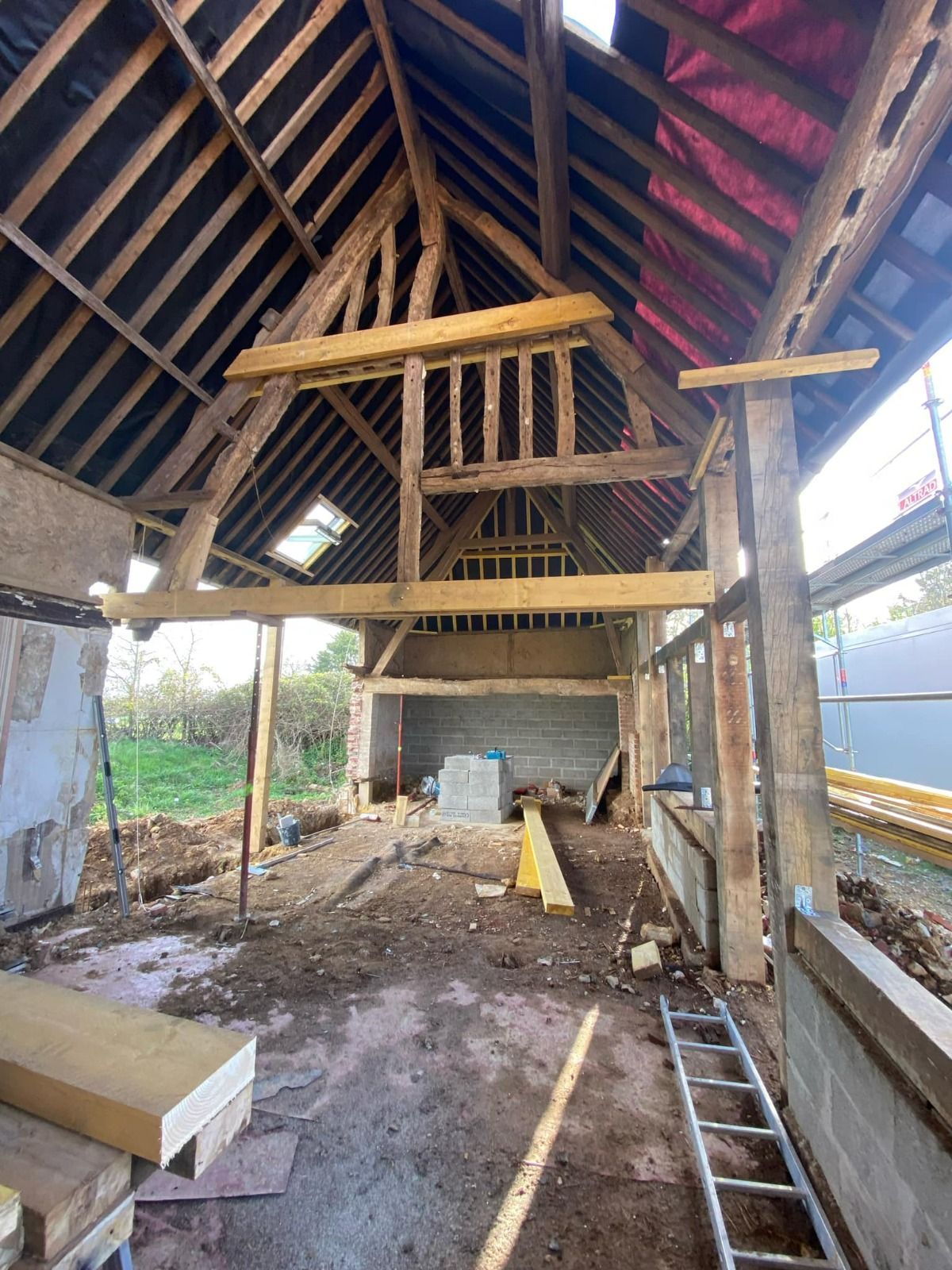 Intérieur d'une grange en rénovation avec poutres apparentes, échelle, bois de construction et grenier partiellement aménagé.