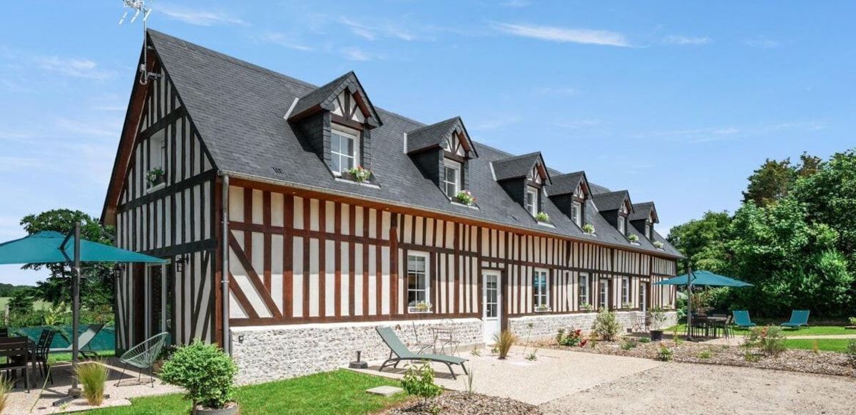 Maison rustique en bois et en pierre, avec des toits gris pentus et un patio sous un ciel bleu.