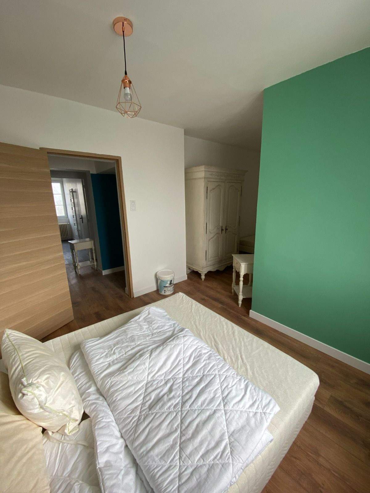 Chambre minimaliste avec lit, parquet, mur d'accent vert, portes de placard coulissantes et porte ouverte