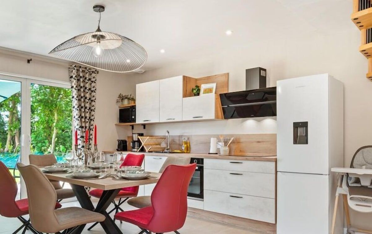 Cuisine moderne et lumineuse avec table à manger, chaises rouges et beiges, placards blancs et grande fenêtre