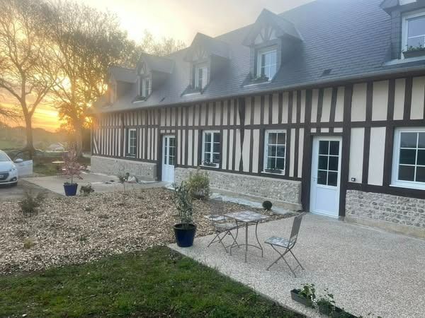 Maison rustique baignée de soleil, avec charpente en bois, soubassement en pierre et patio aménagé avec chaises et plantes en pot au coucher du soleil
