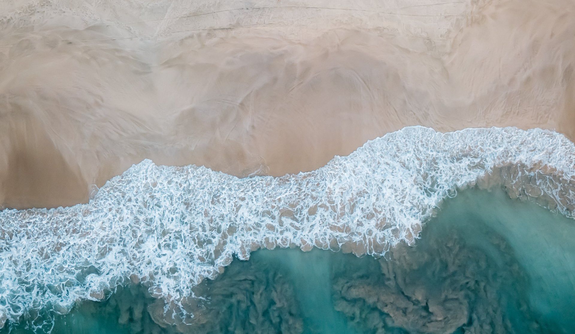 An aerial view of a wave crashing on a sandy beach.