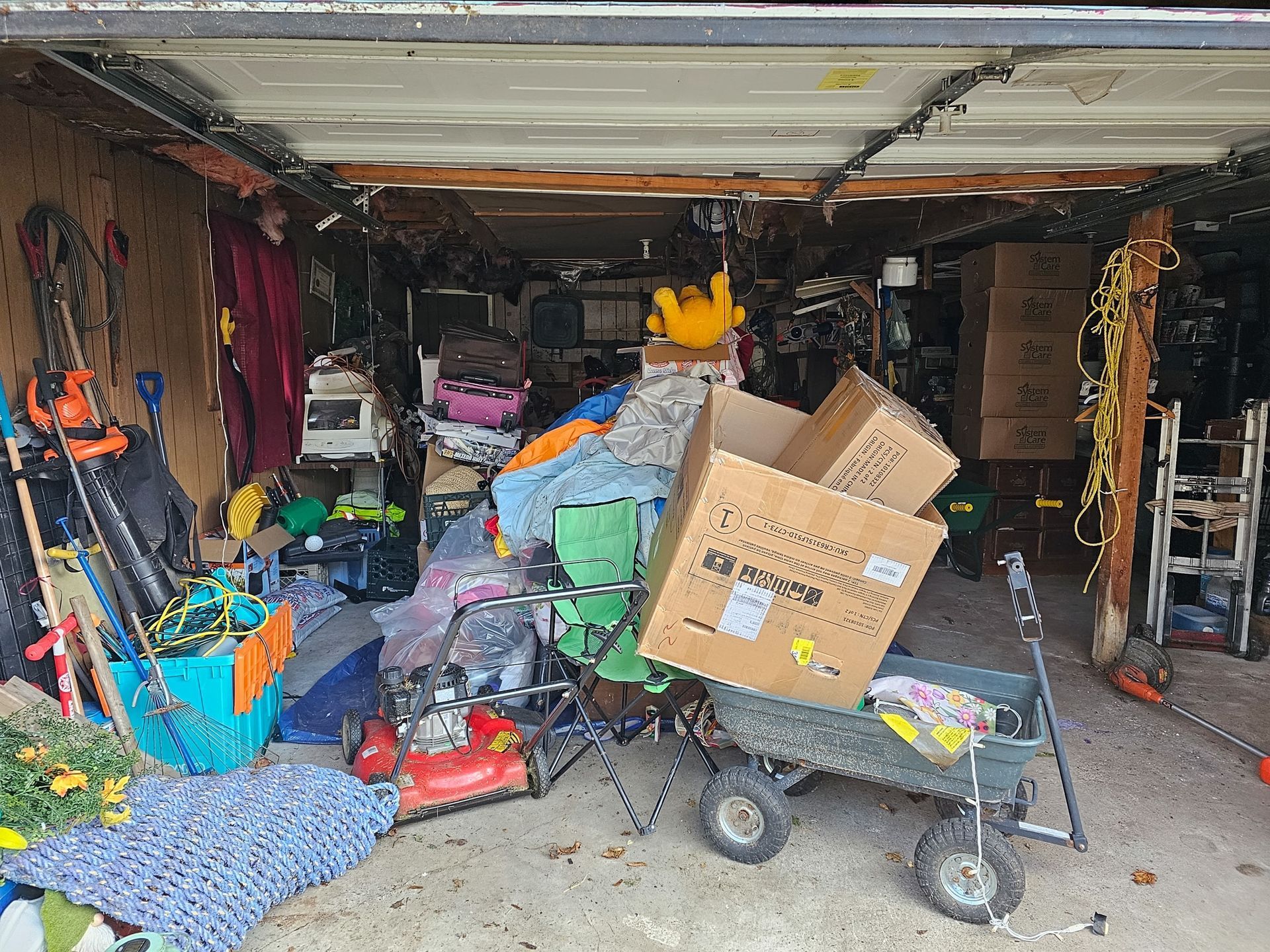 Cluttered garage packed with boxes, tools, and assorted household items stacked across the floor.