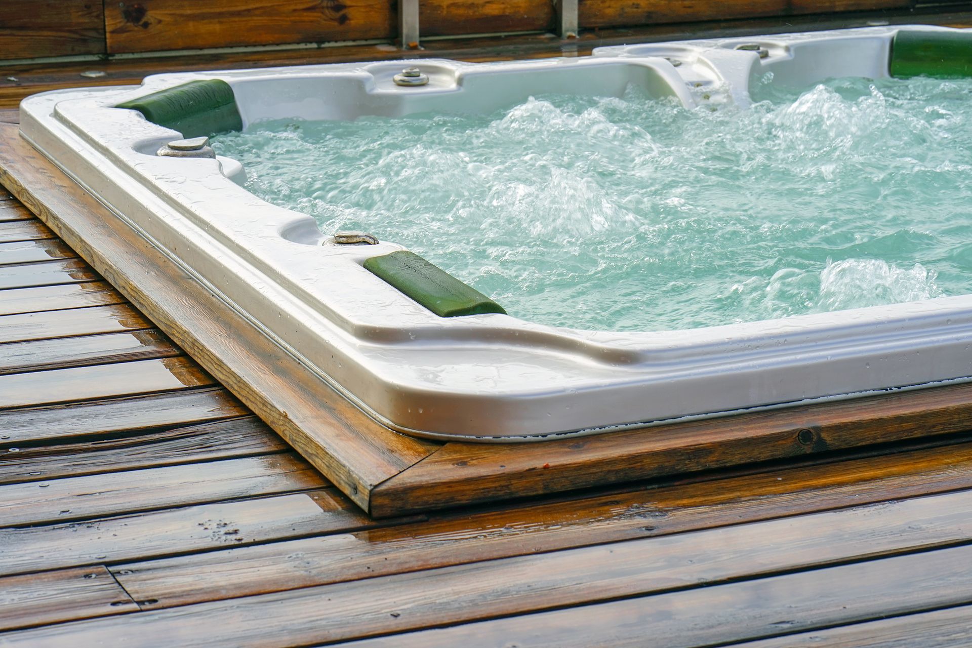 Wooden deck beside a bubbling outdoor hot tub with a white rim and green water