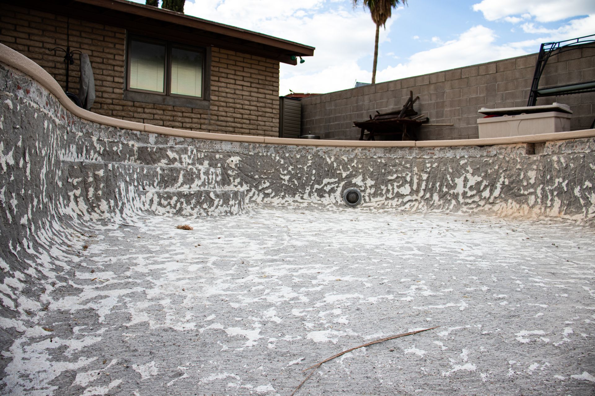 Empty weathered swimming pool with peeling white coating in a backyard courtyard.
