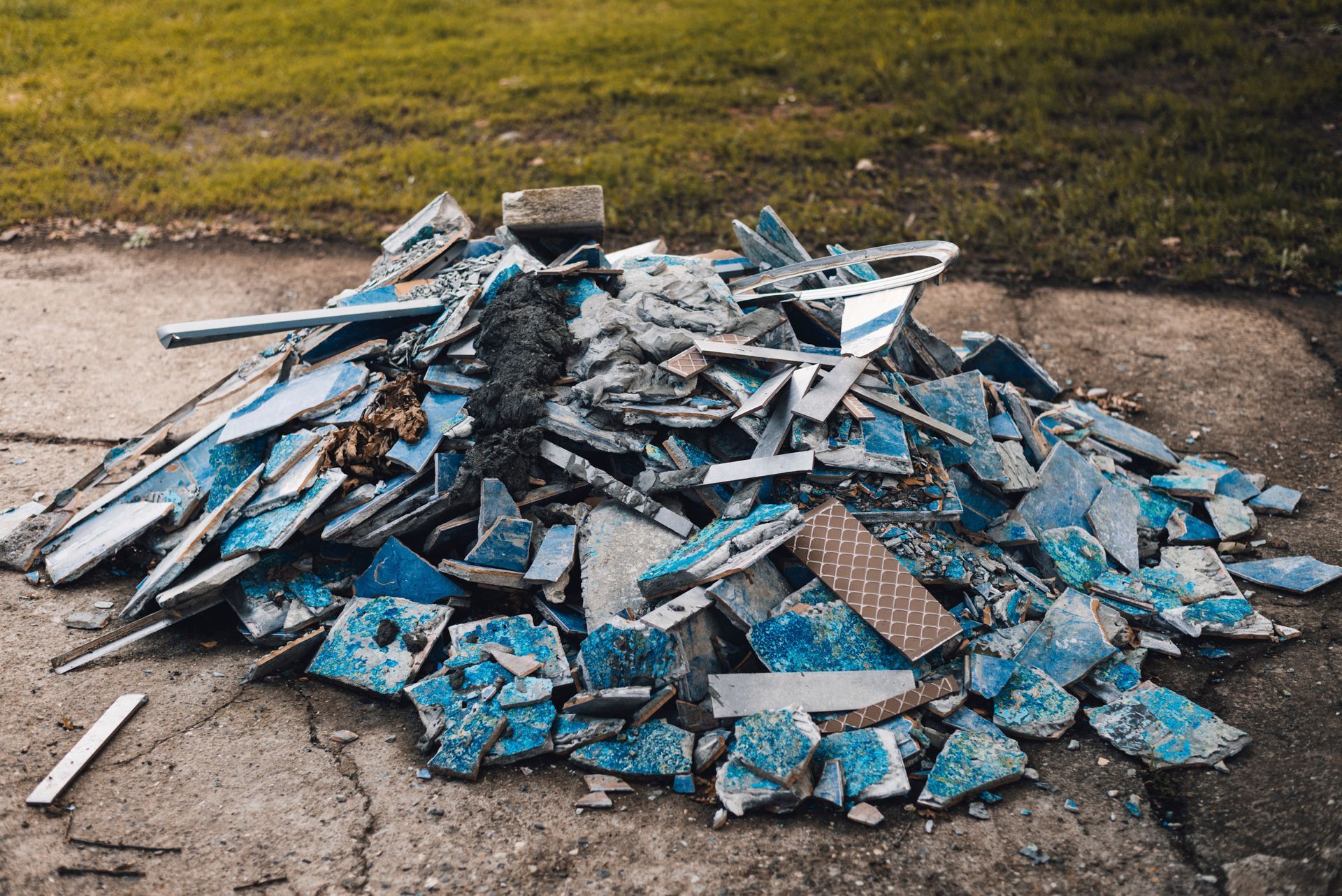Pile of broken blue and white concrete debris on a pavement beside a grassy verge