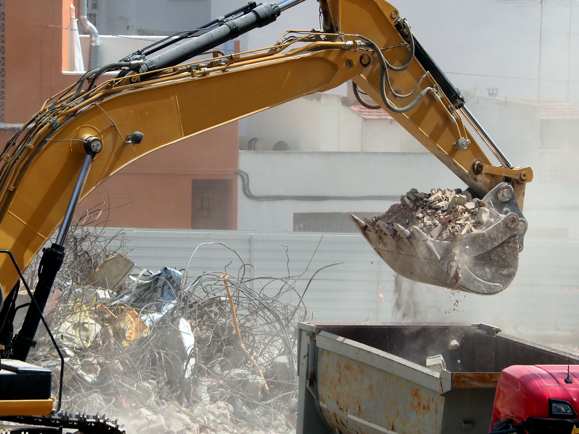 Excavator loading rubble into a dumpster at a demolition site