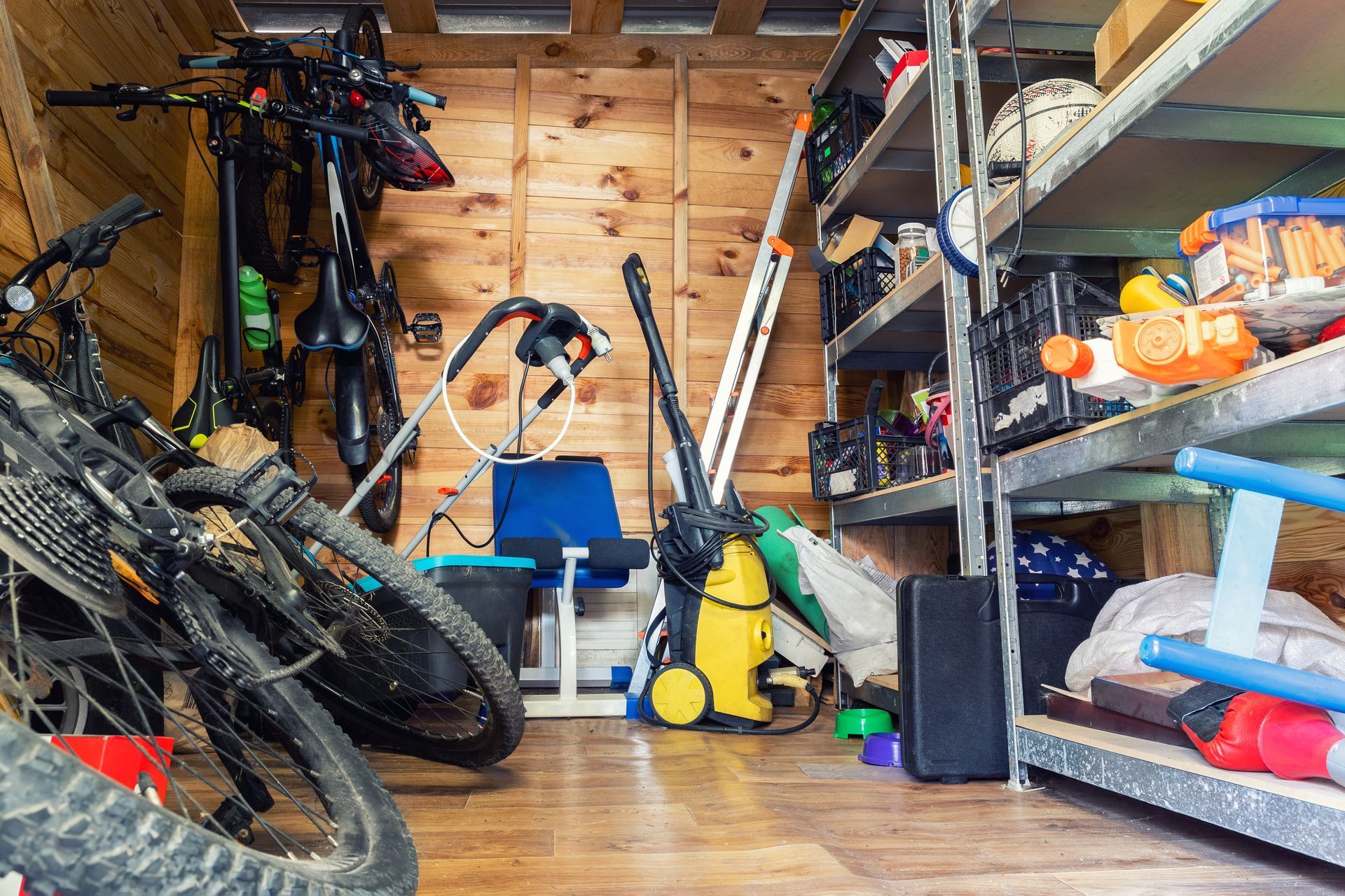 A cluttered garage with bicycles, tools, and shelves of stored items.