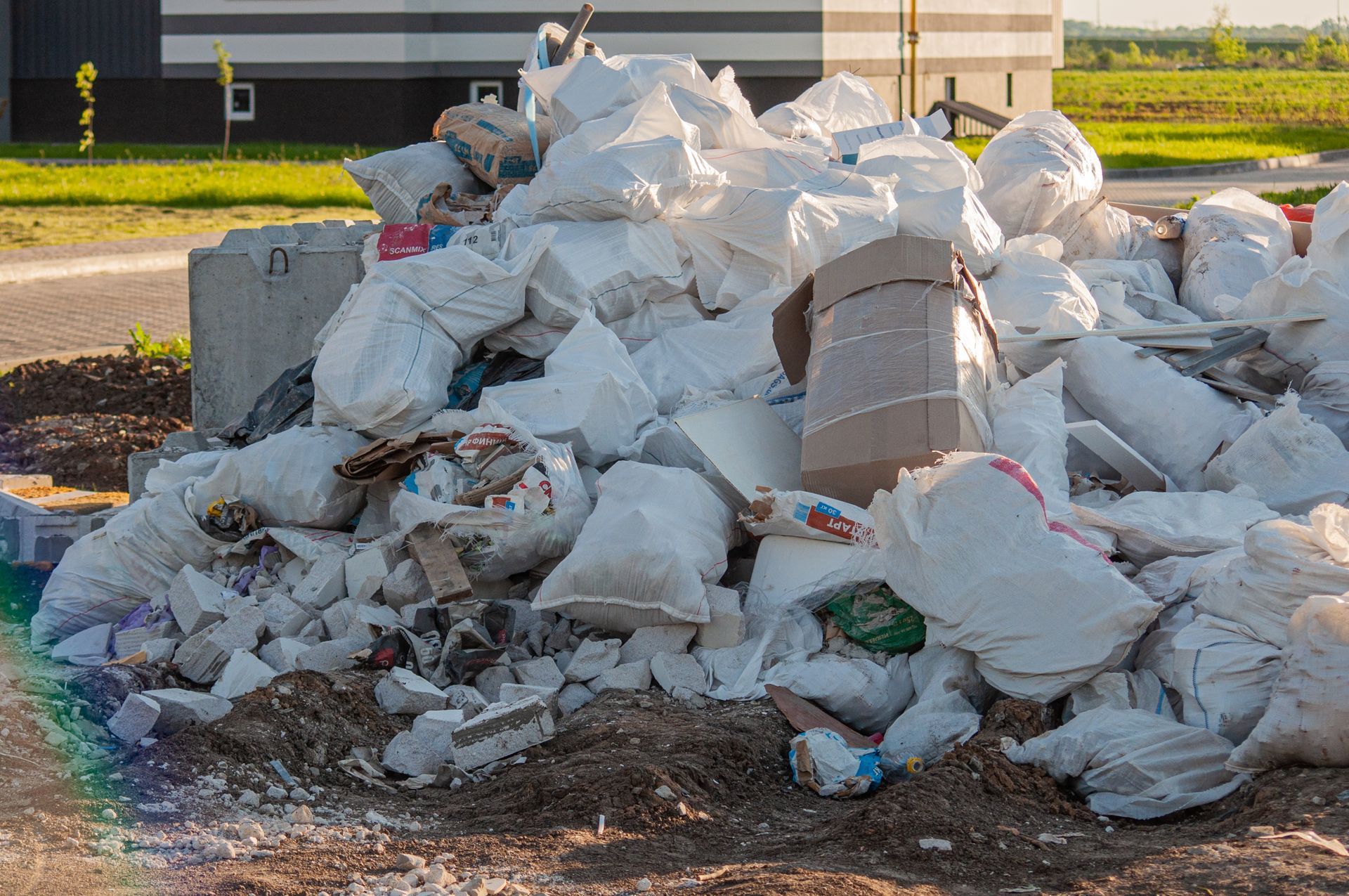 Pile of trash bags and rubble stacked outdoors near a street in daylight
