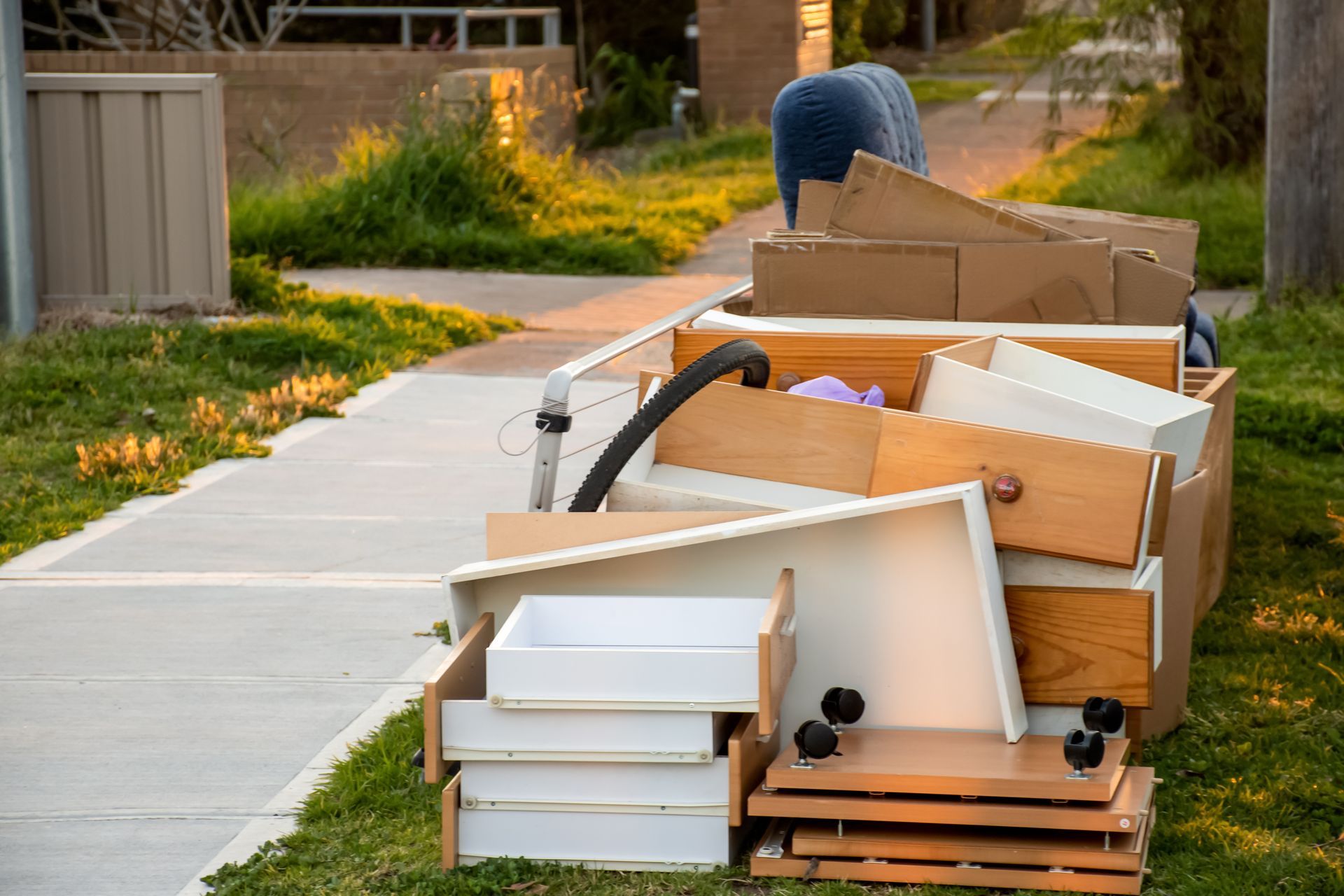 Pile of discarded furniture and boxes on a sidewalk beside a residential curb.