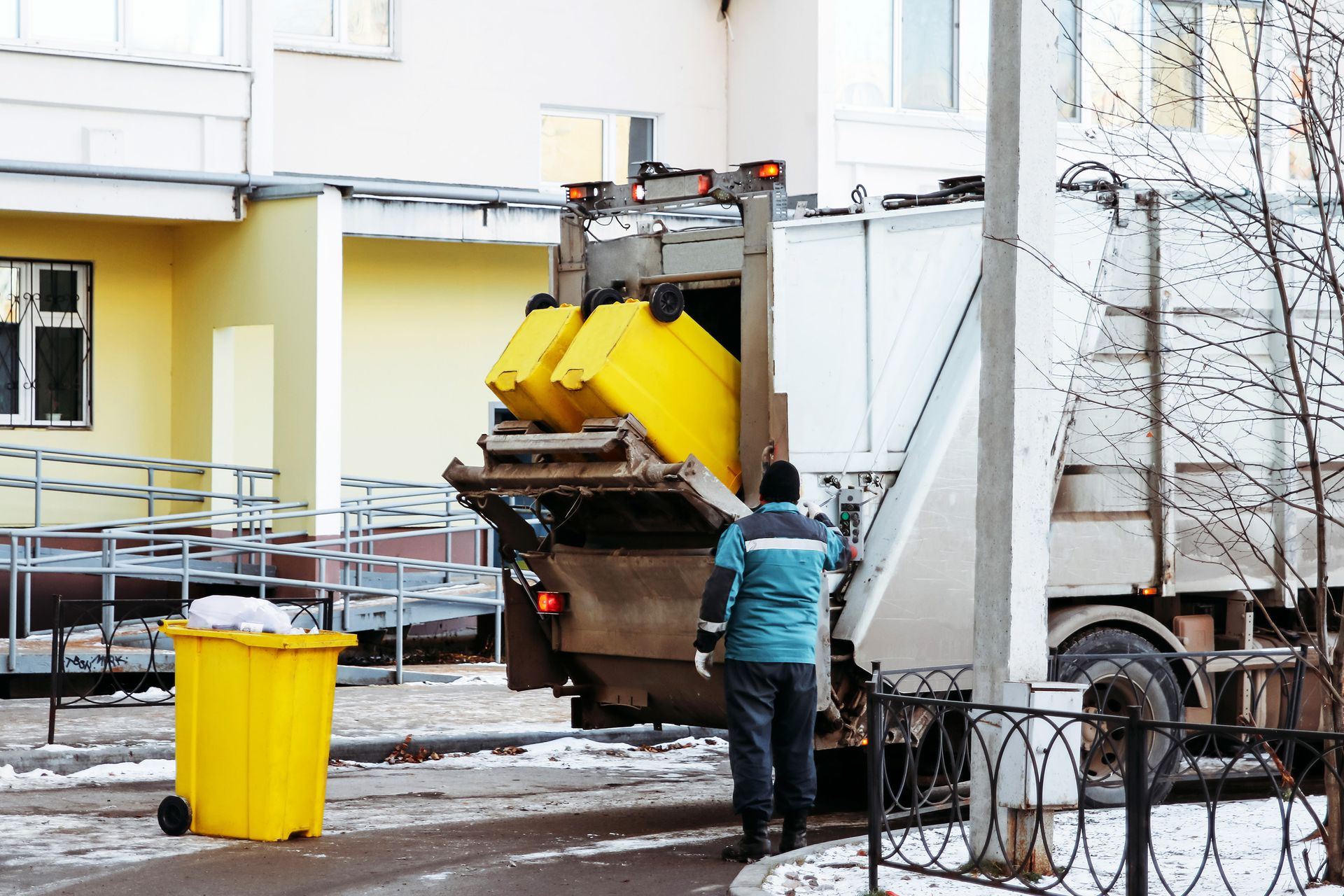 Sanitation worker emptying yellow bins into a garbage truck on a snowy street