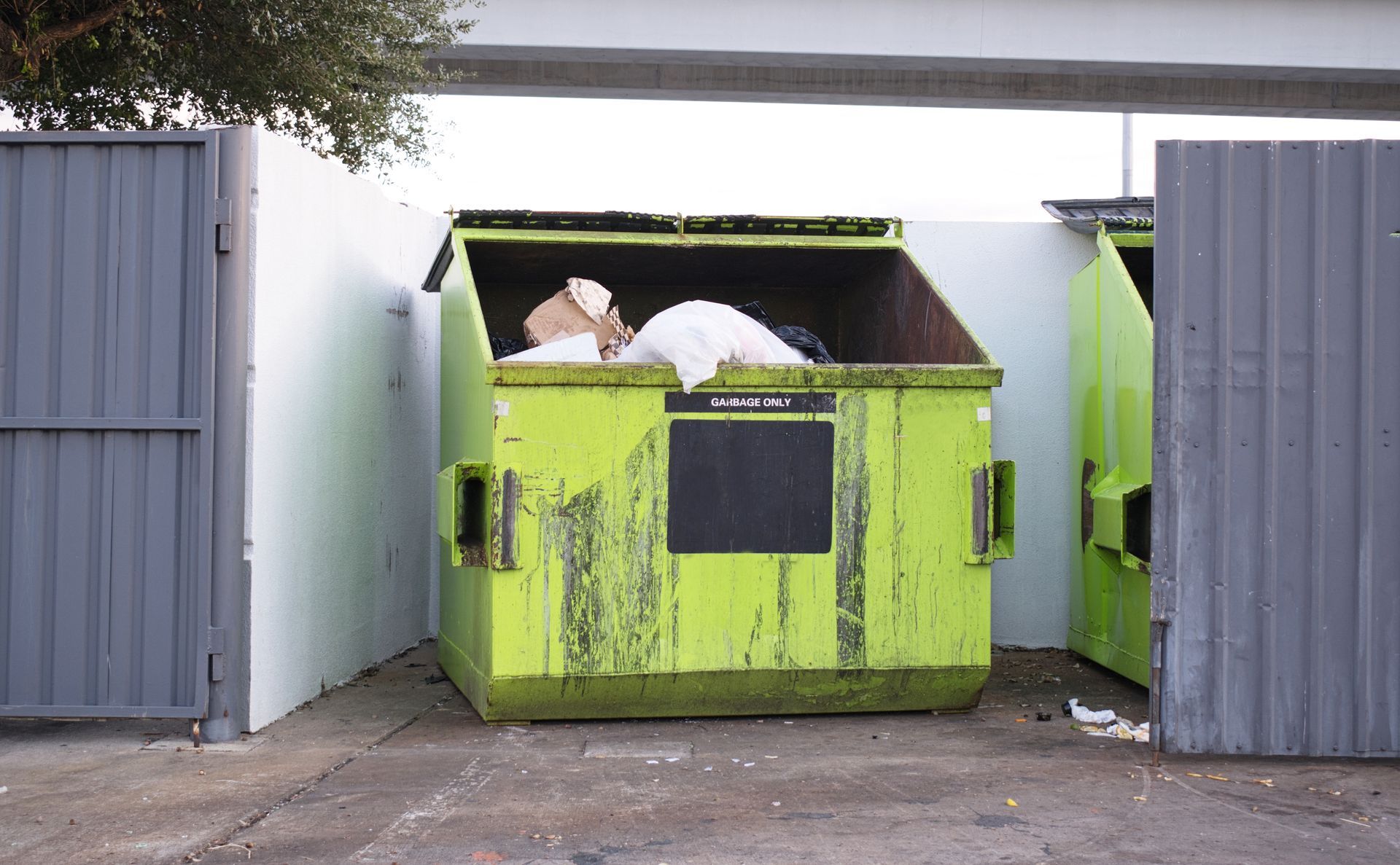 Bright green recycling bin between gray metal containers, with white trash visible inside.