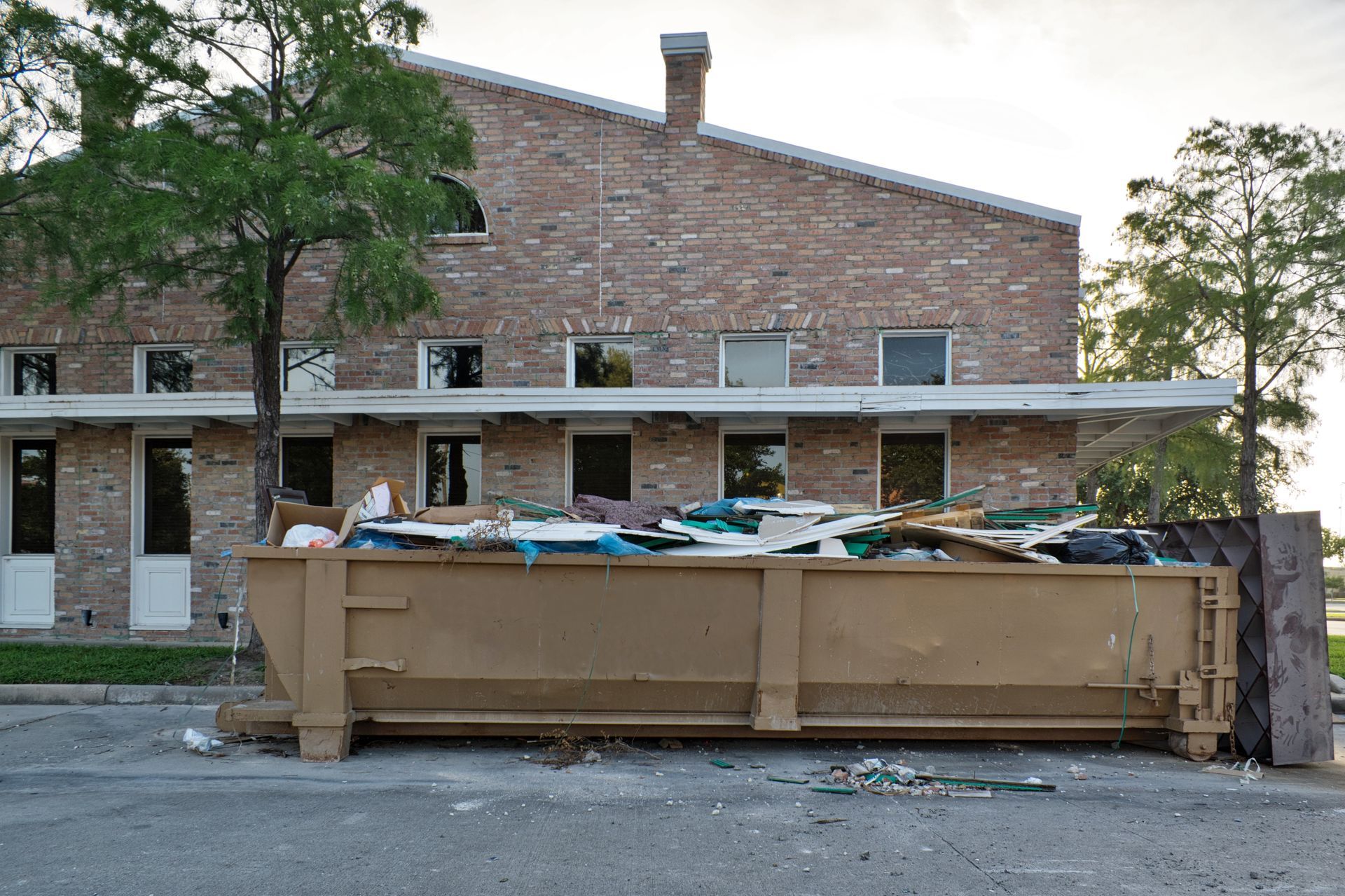Large dumpster filled with debris in front of a brick building under construction or demolition