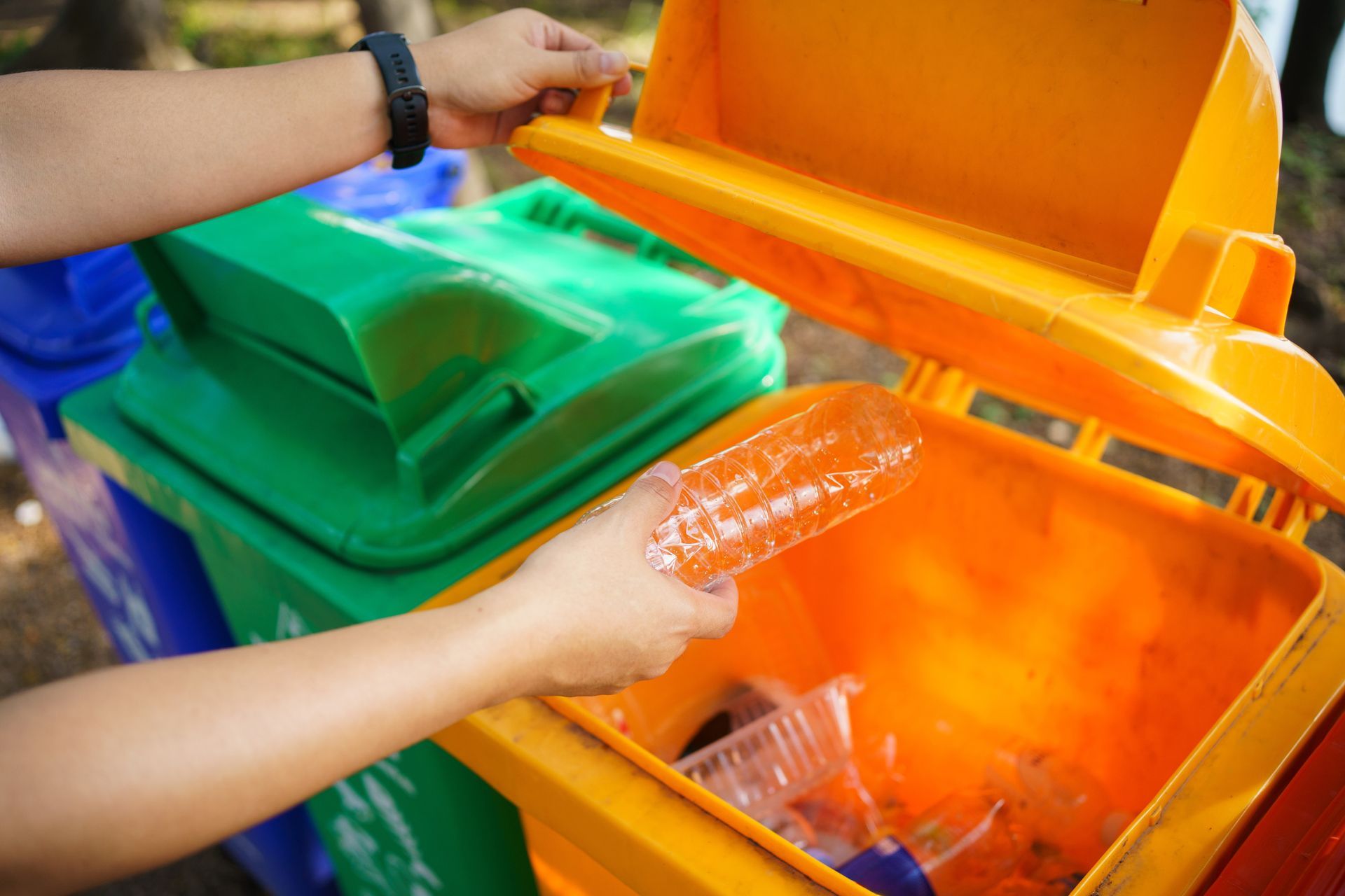 Hands sorting recyclables into orange and green bins outdoors