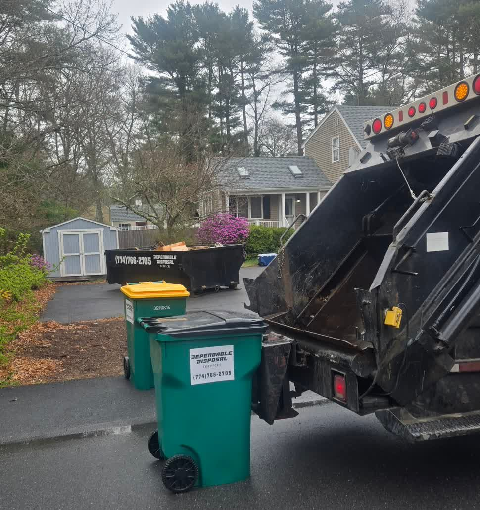 Trash truck emptying a green bin in a driveway on a cloudy suburban street