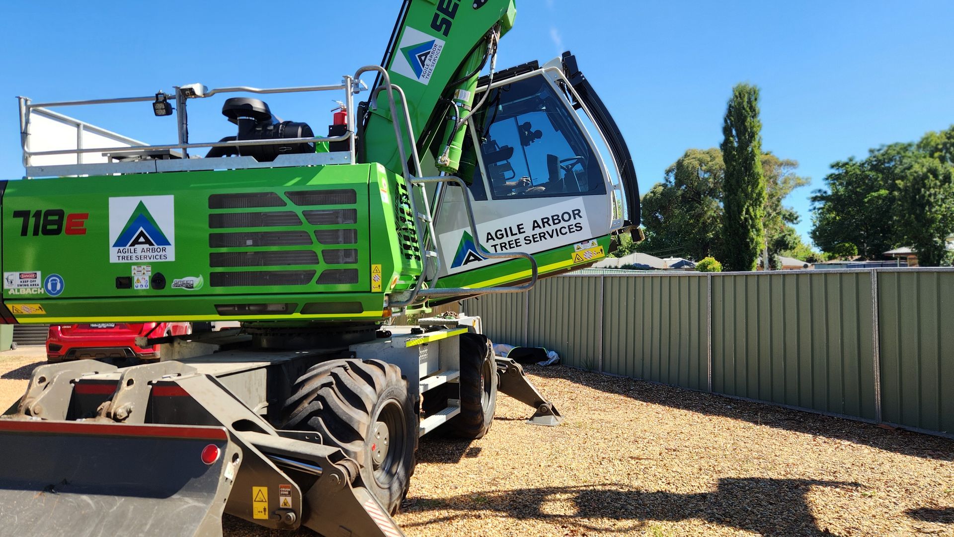 A bright green Sennebogen 718K material handler sits on a gravel lot next to a green fence under a clear blue sky.