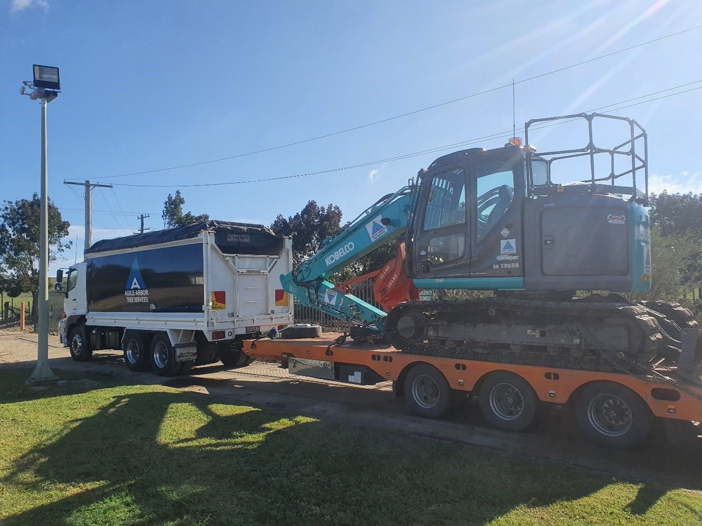 Truck Towing Excavator on a Trailer on a Grassy Area, Blue Sky — Agile Arbor Pty Limited in Oberon, NSW