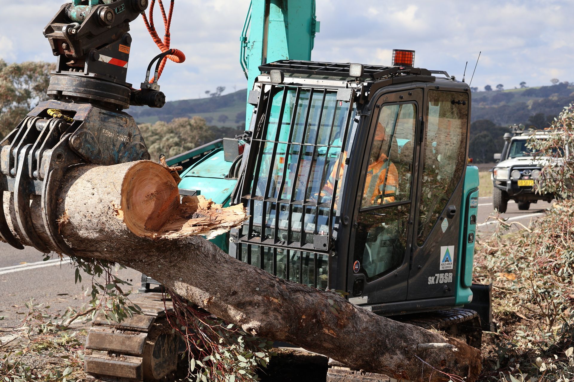 Excavator gripping a large log, clearing debris from a roadside — Agile Arbor Pty Limited in Blue Mountains, NSW