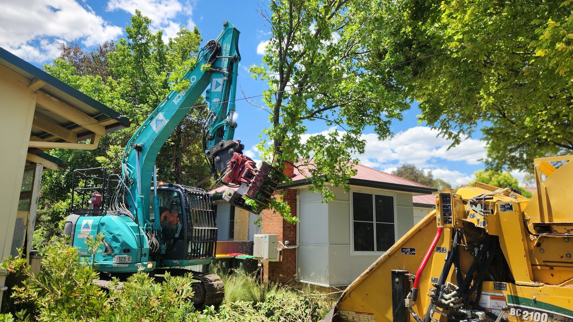 Excavator cutting down a tree next to a house, with a wood chipper present — Agile Arbor Pty Limited in Kelso, NSW