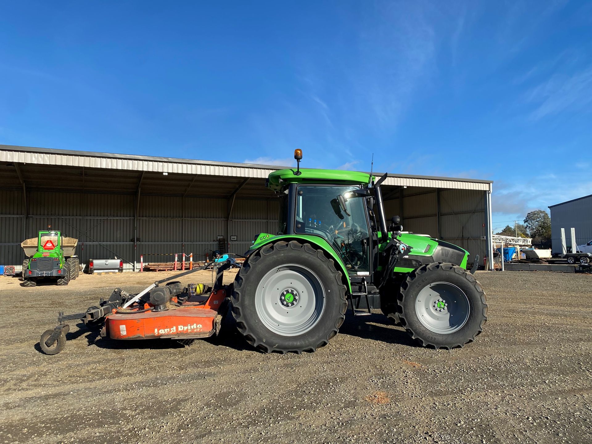Green tractor with attached orange mower parked on gravel in front of a shed — Agile Arbor Pty Limited in Kelso, NSW