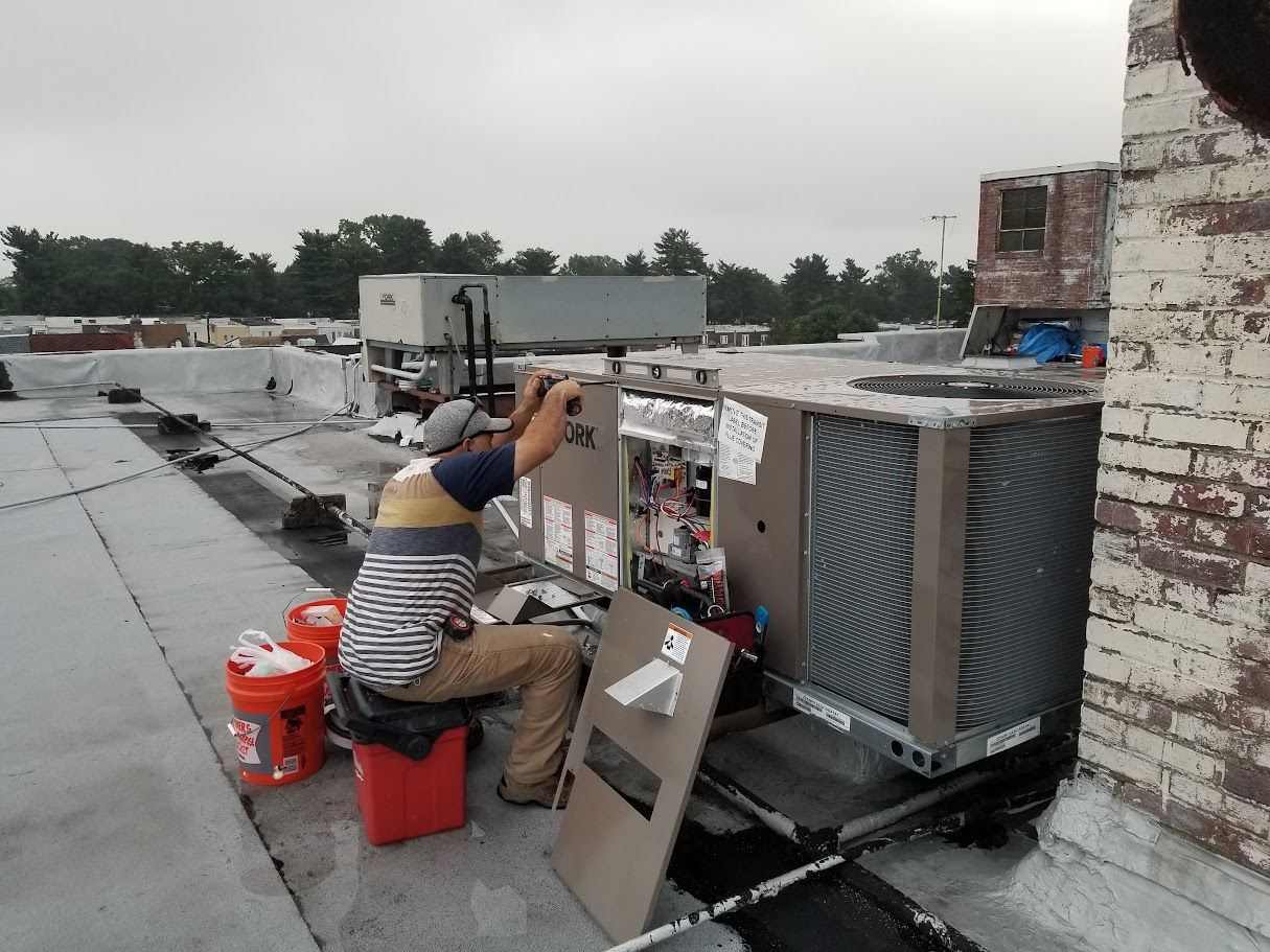 A man is working on an air conditioner on the roof of a building.