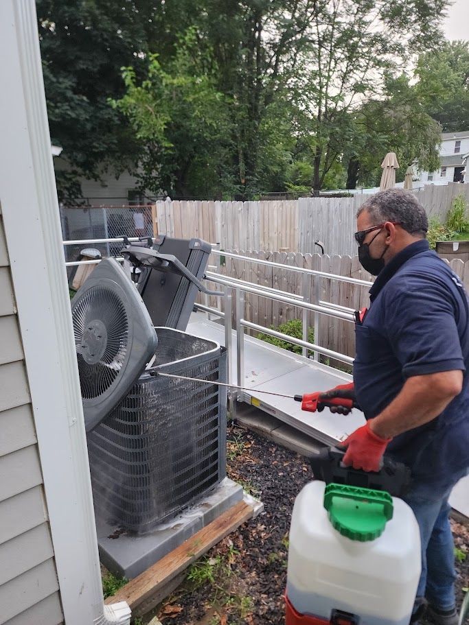 A man wearing a mask is spraying insecticide on an air conditioner.