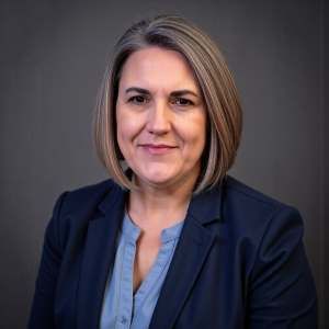 A woman in a blue jacket and blue shirt is smiling for the camera.