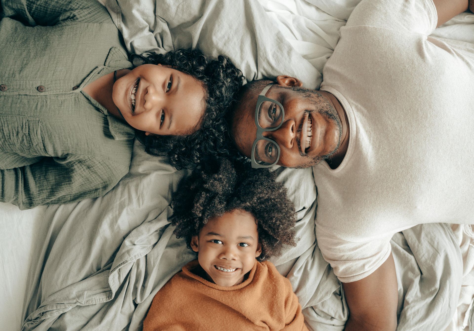 A family is sitting on a bed with a little girl blowing soap bubbles.