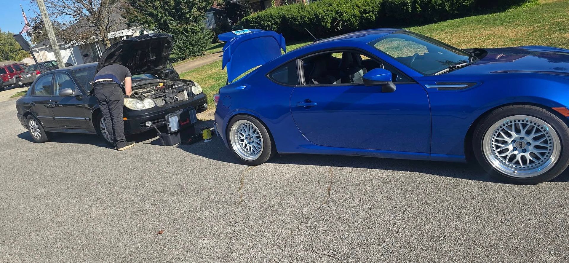 A man is working on the engine of a blue sports car.