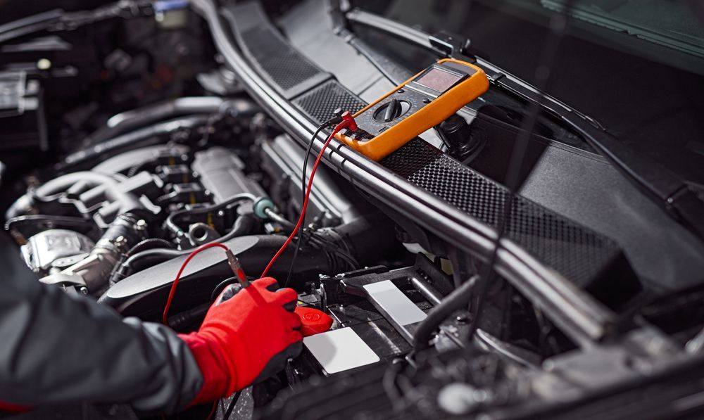 A mechanic is working on a car engine with a multimeter.