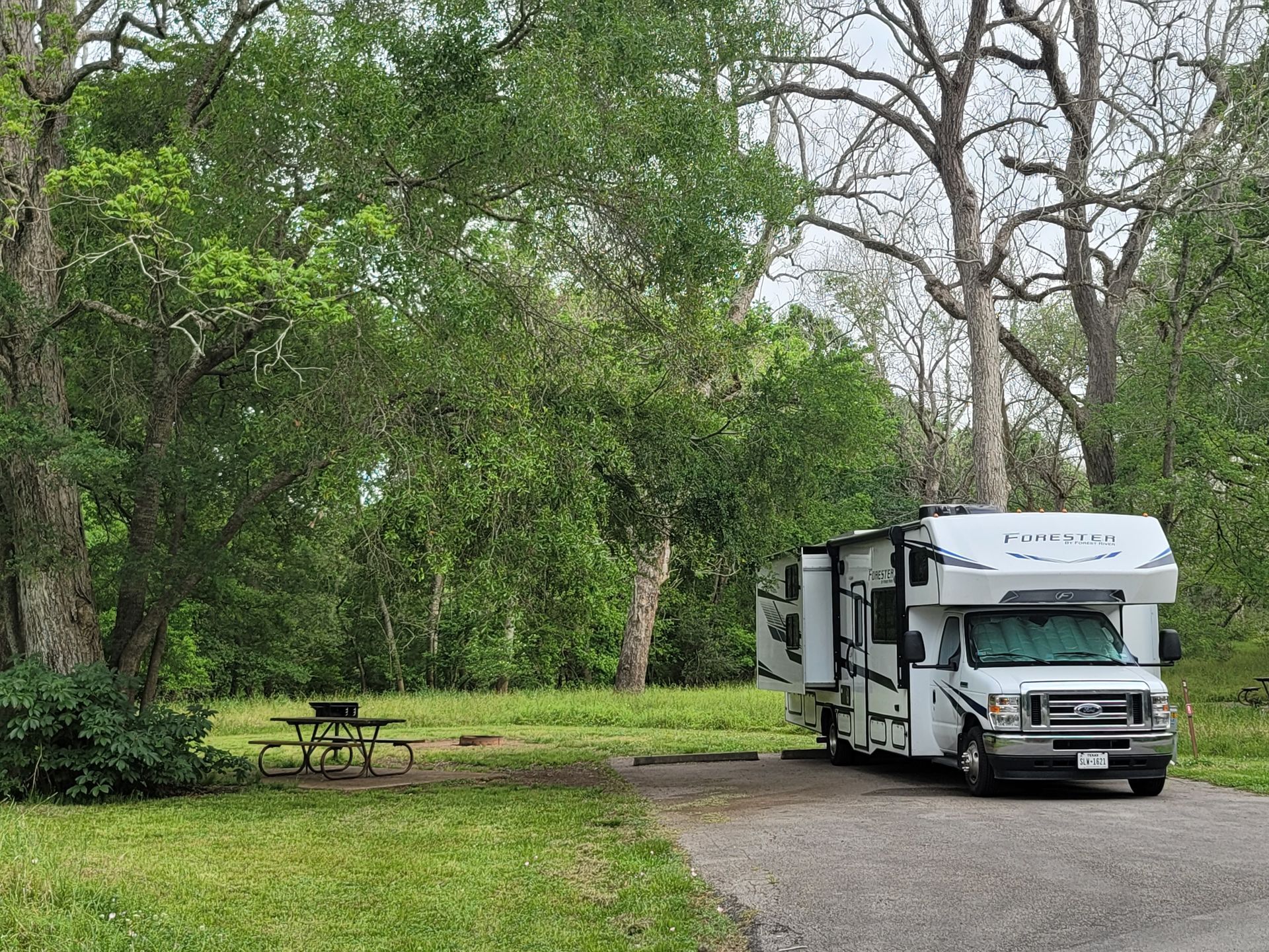 a rv is parked in a parking lot next to a picnic table .