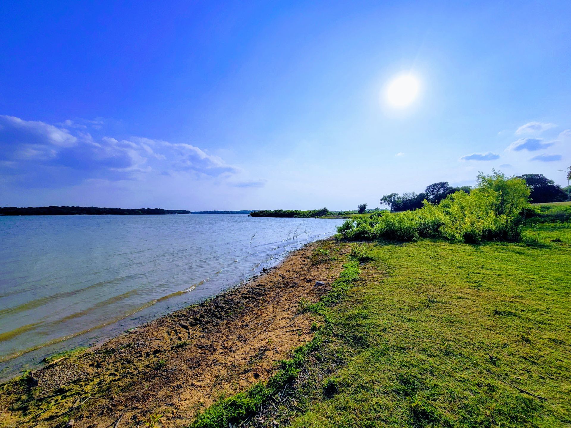 a large body of water surrounded by grass and trees on a sunny day .