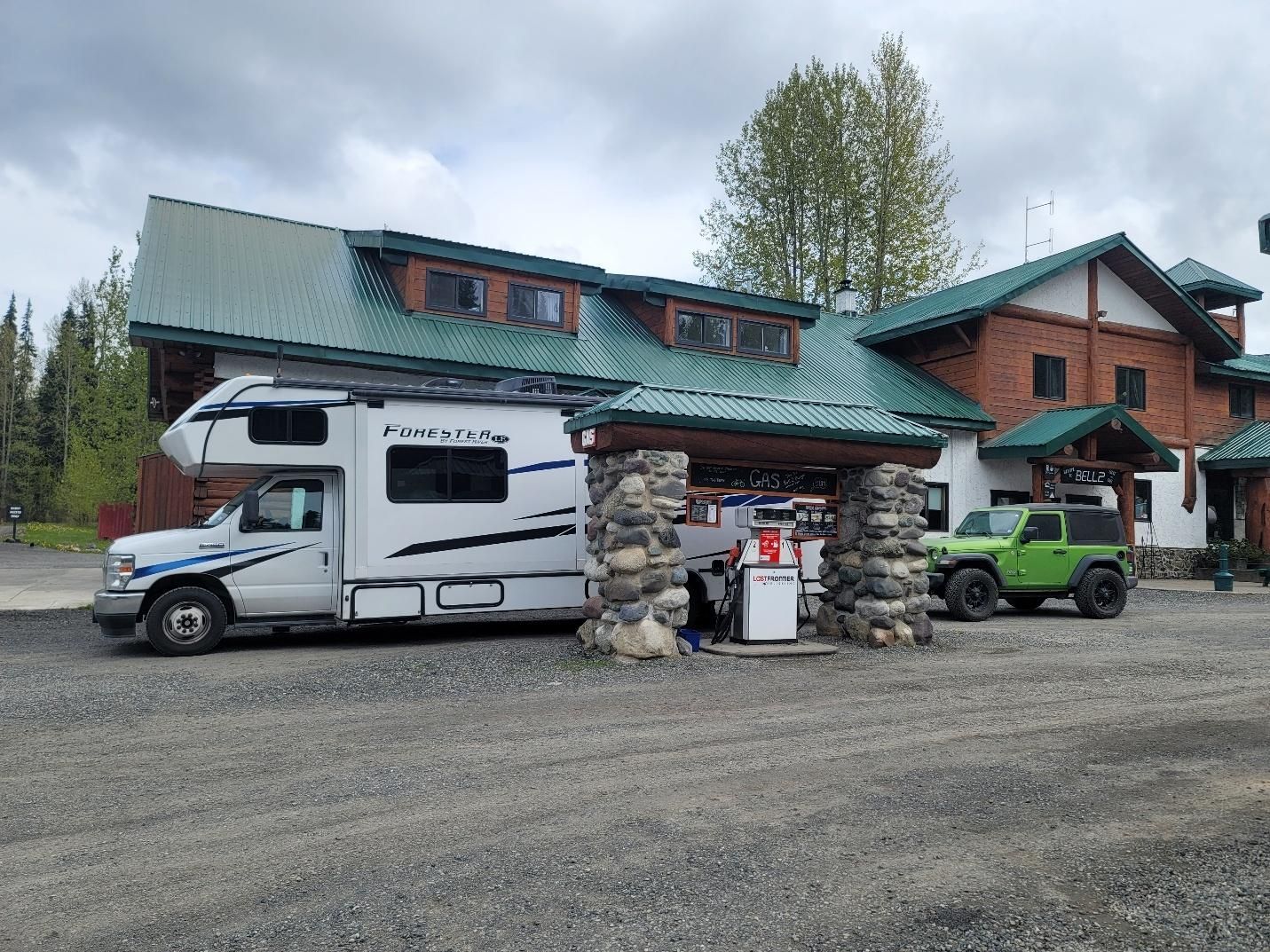 Forest River Forester motorhome towing a green Jeep Wrangler refueling at the Bell 2 Lodge on the Cassiar highway.