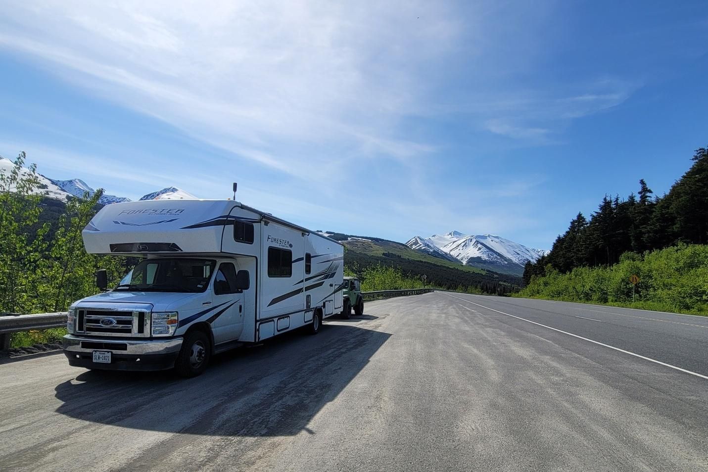 A car and RV at a gas station with a yellow and green canopy, under a cloudy sky.