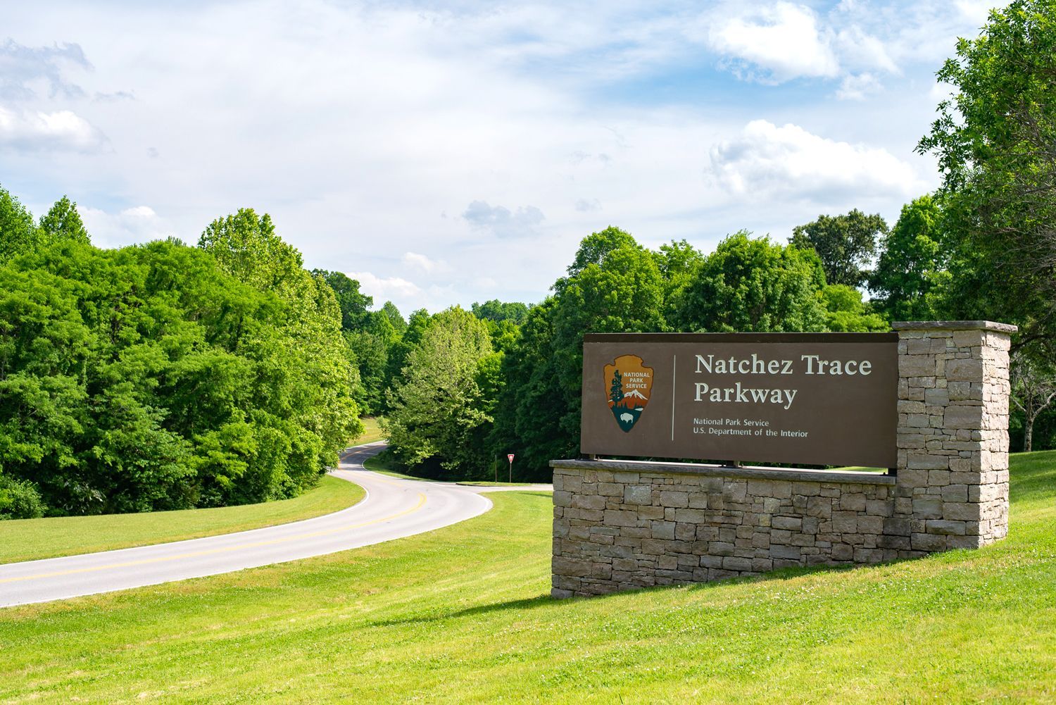 a sign for Natchez Trace Parkway is in the middle of a grassy field.