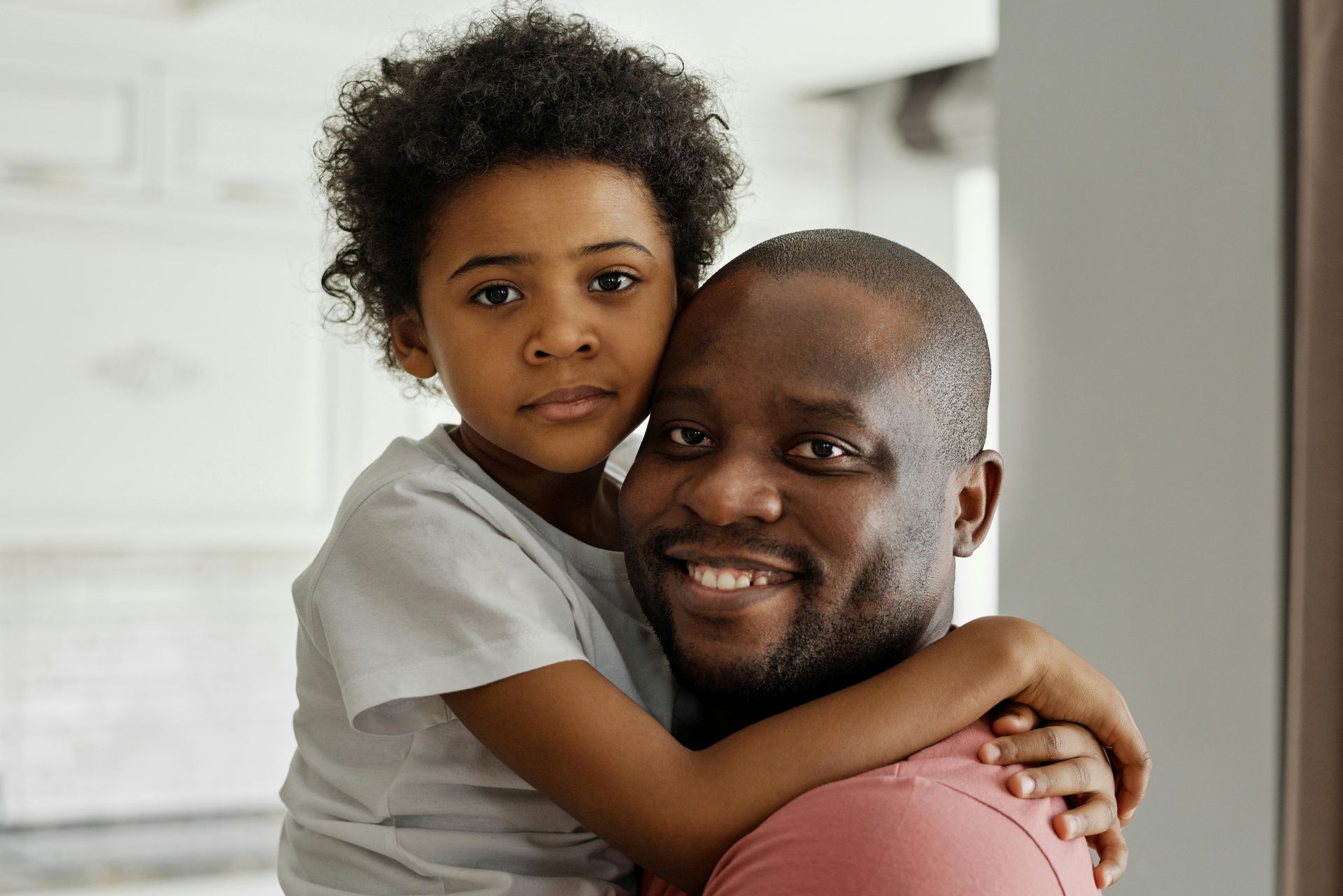 A parent smiling warmly while holding their child close in a bright indoor setting.