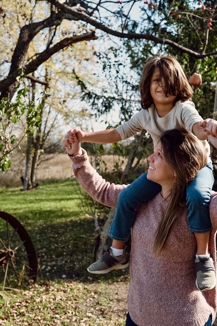 A woman is carrying a child on her shoulders in an orchard.