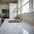 White kitchen with a stainless steel sink, faucet, and appliances, bright counter, and window.