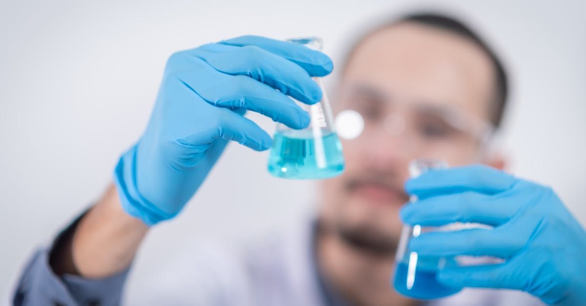 A man in blue gloves is holding a beaker of blue liquid.