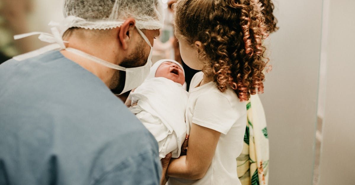 A man and a little girl are holding a newborn baby in a hospital room.