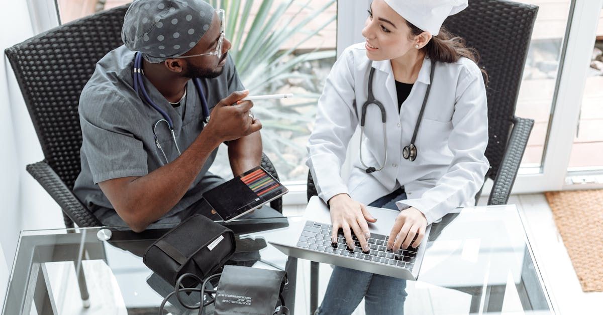 A doctor and a nurse are sitting at a table with a laptop.